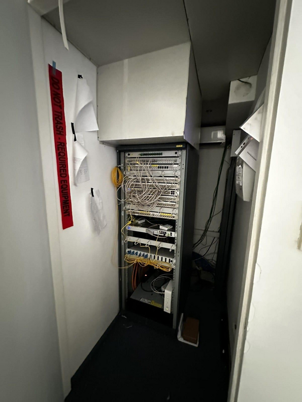 Ein schmaler Raum mit einem Netzwerk-Serverschrank, in dem zahlreiche Kabel und Geräte installiert sind.