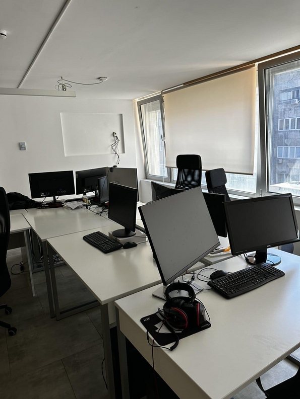 Mehrere leere Arbeitsplätze mit Computern und Kopfhörern, die in einem Raum mit großen Fenstern stehen.