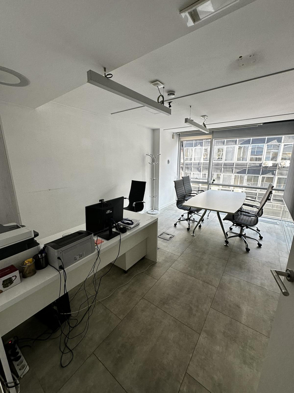Ein leerer Büroraum mit einem Schreibtisch und Computertechnik, mehrere Kabel sind offen verlegt, mit großen Fenstern im Hintergrund.